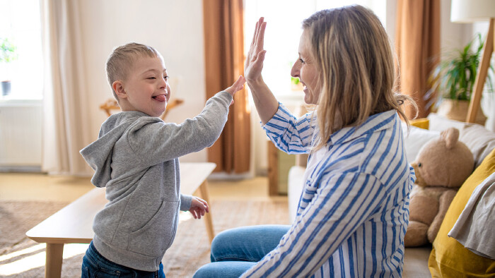 © Halfpoint, stock.adobe.com Eine fröhliche, junge Mama spielt mit ihrem Sohn mit Downsyndrom zu Hause