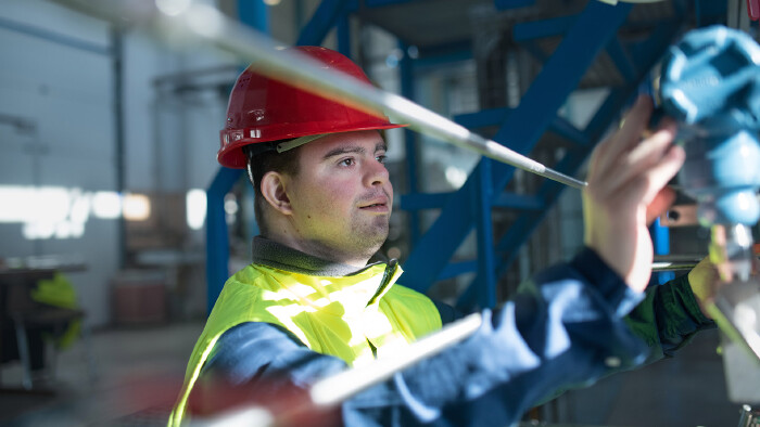 © Halfpoint, stock.adobe.com Junger Arbeiter mit Schutzhelm in einer Fabrik
